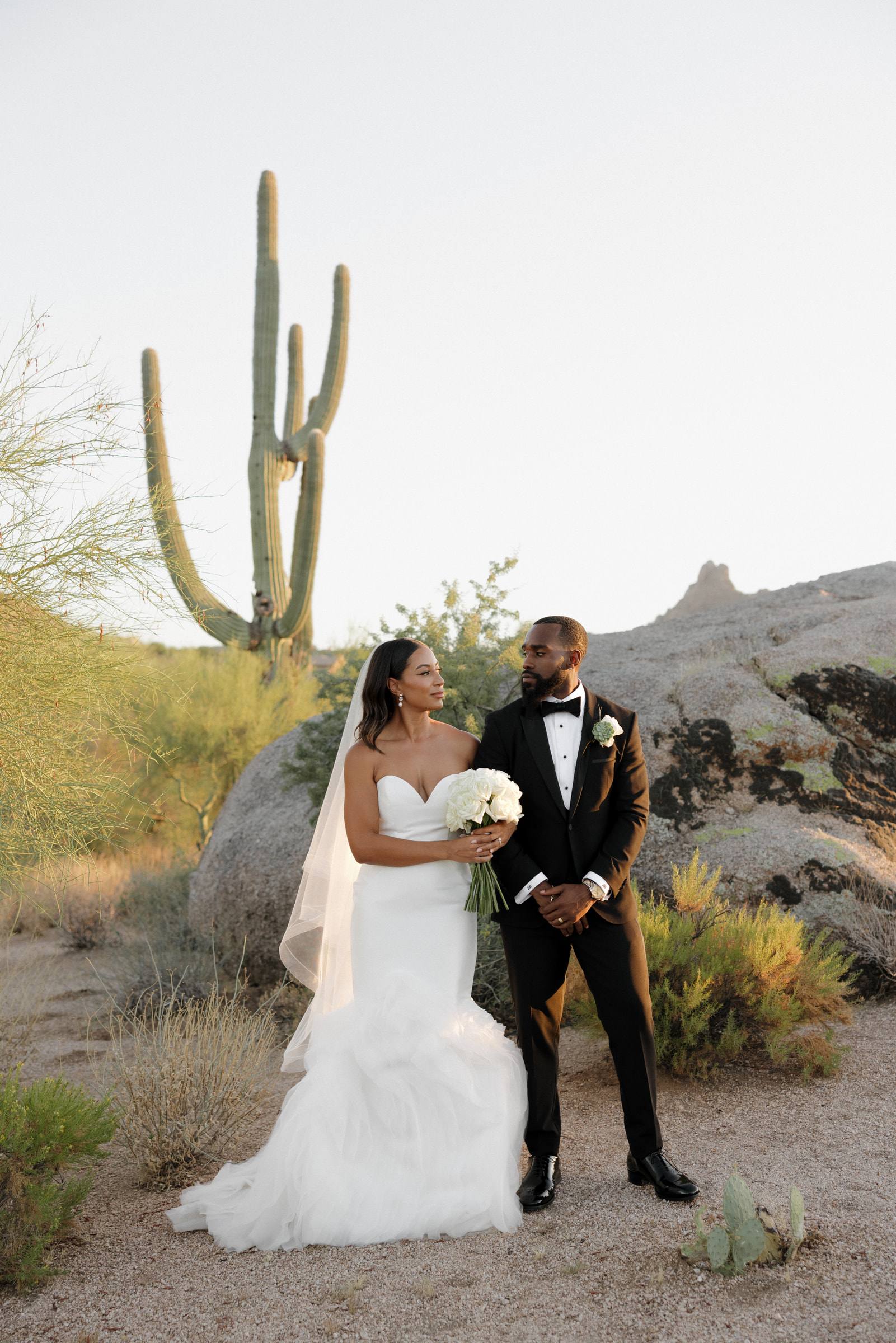 A bride and groom standing among desert boulders and saguaro cactus
