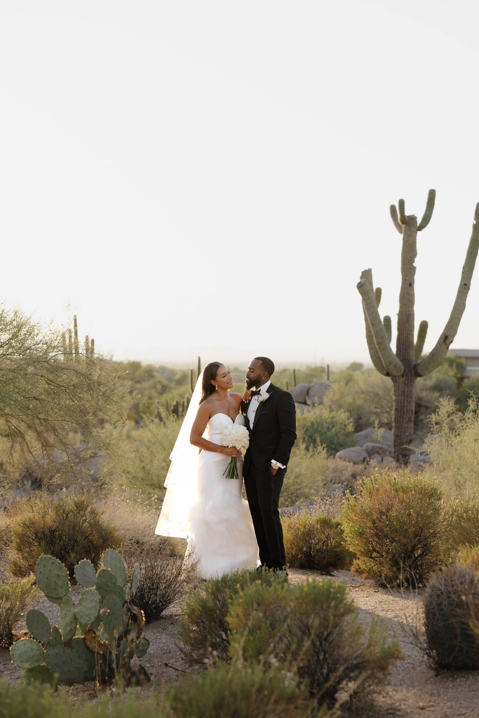 A bride and groom beside a saguaro cactus at golden hour