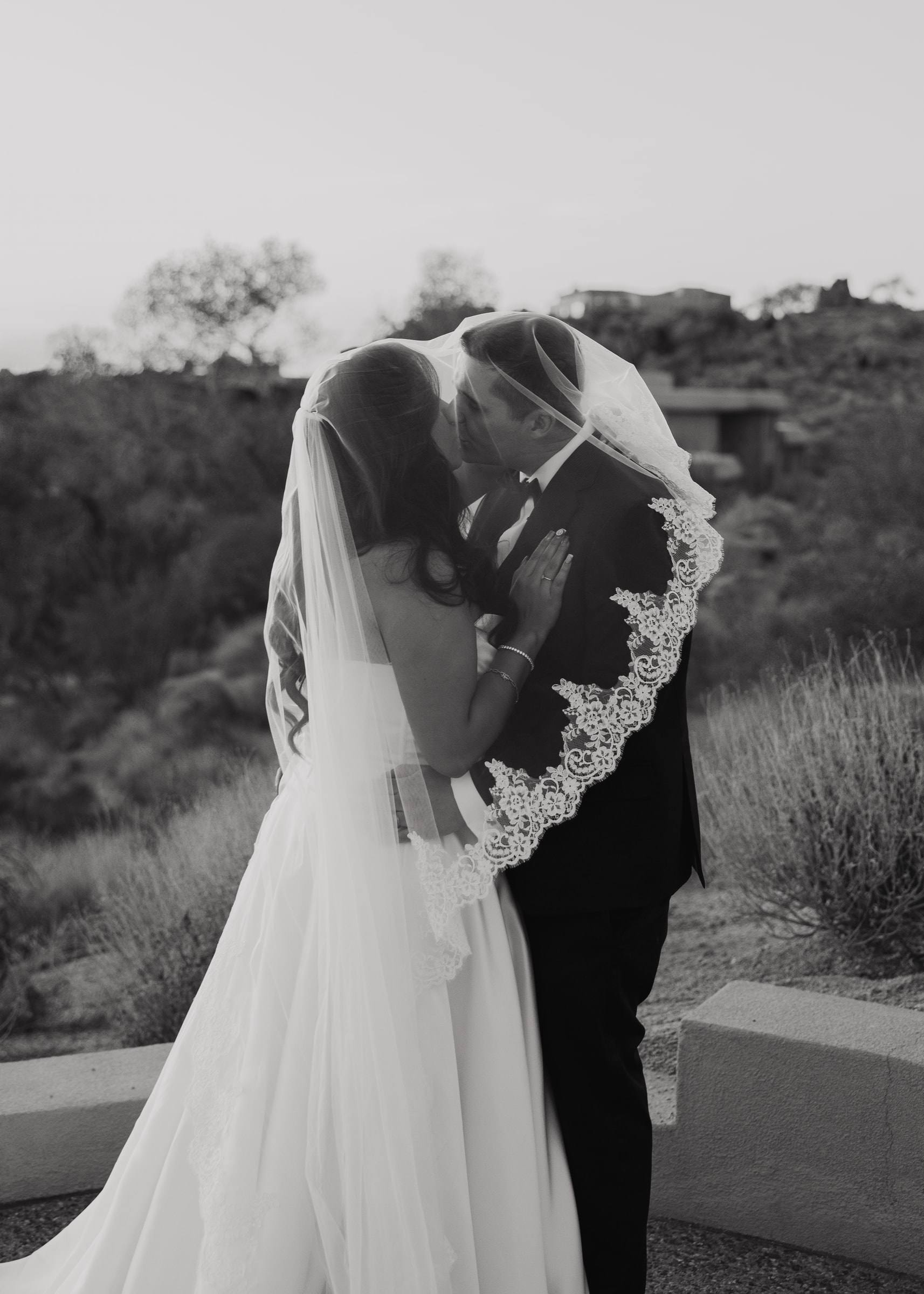 A bride and groom kissing beneath her lace-edged veil in the Arizona desert, in black and white