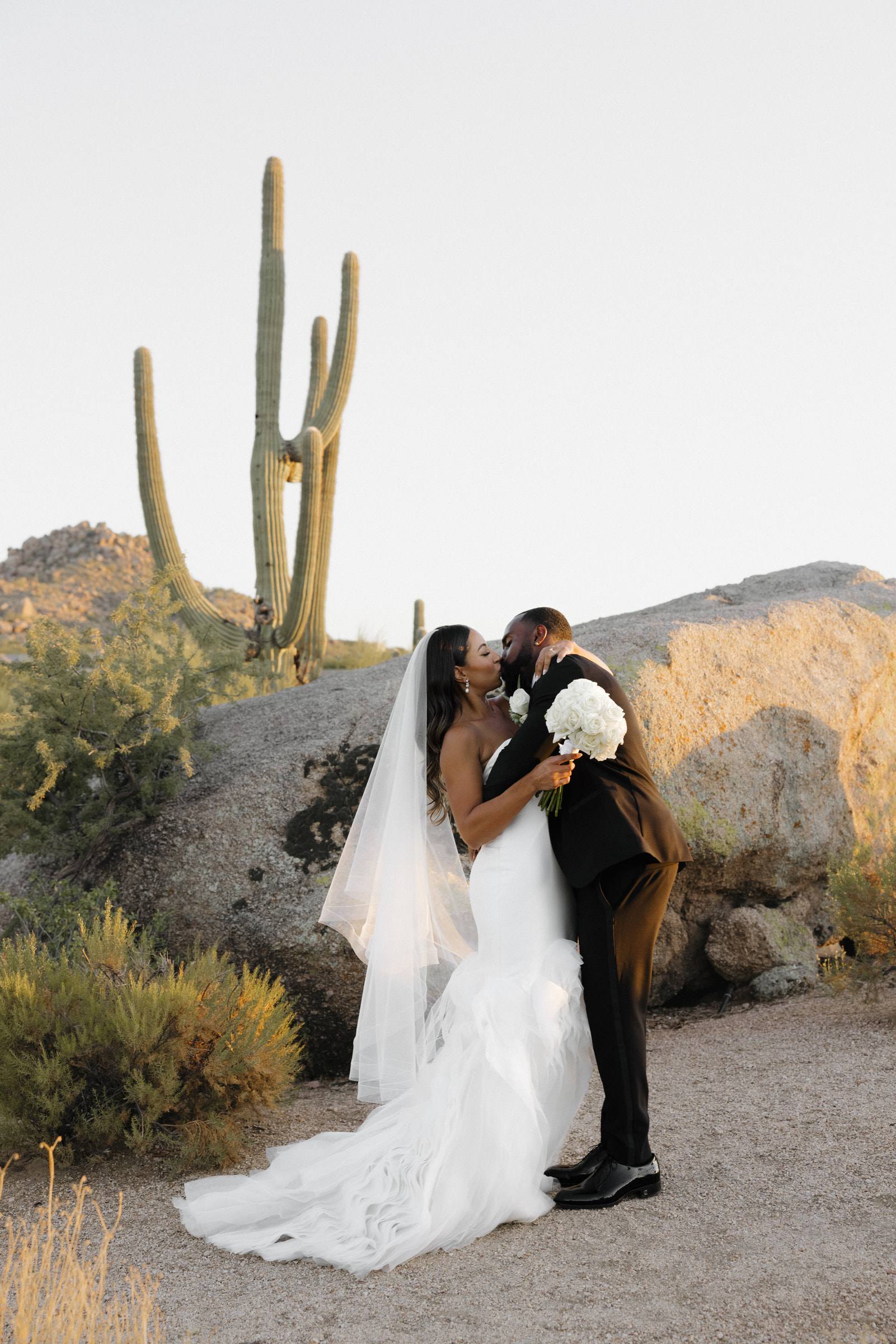 A bride and groom kissing beneath a saguaro cactus in the Arizona desert