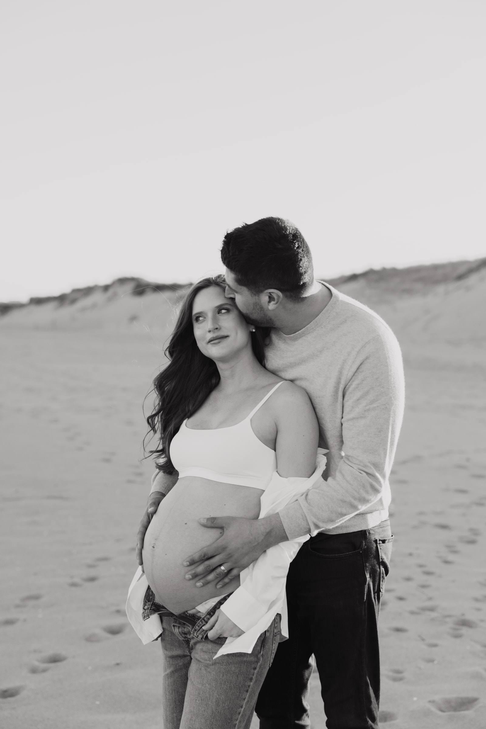 An expecting couple embracing on the beach, in black and white