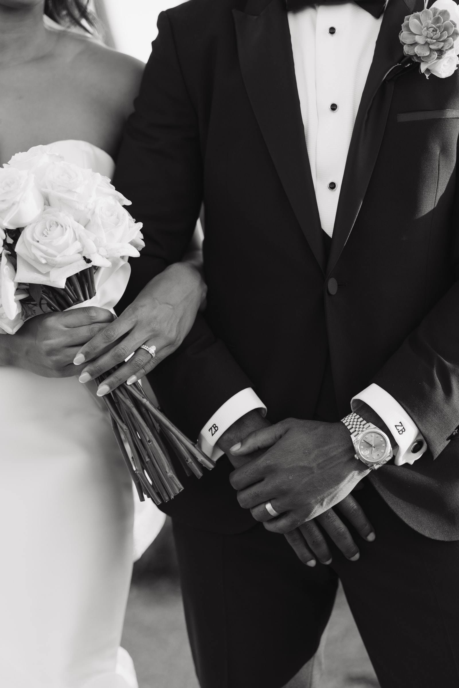 Close detail of a bride’s bouquet and a groom’s hands, in black and white