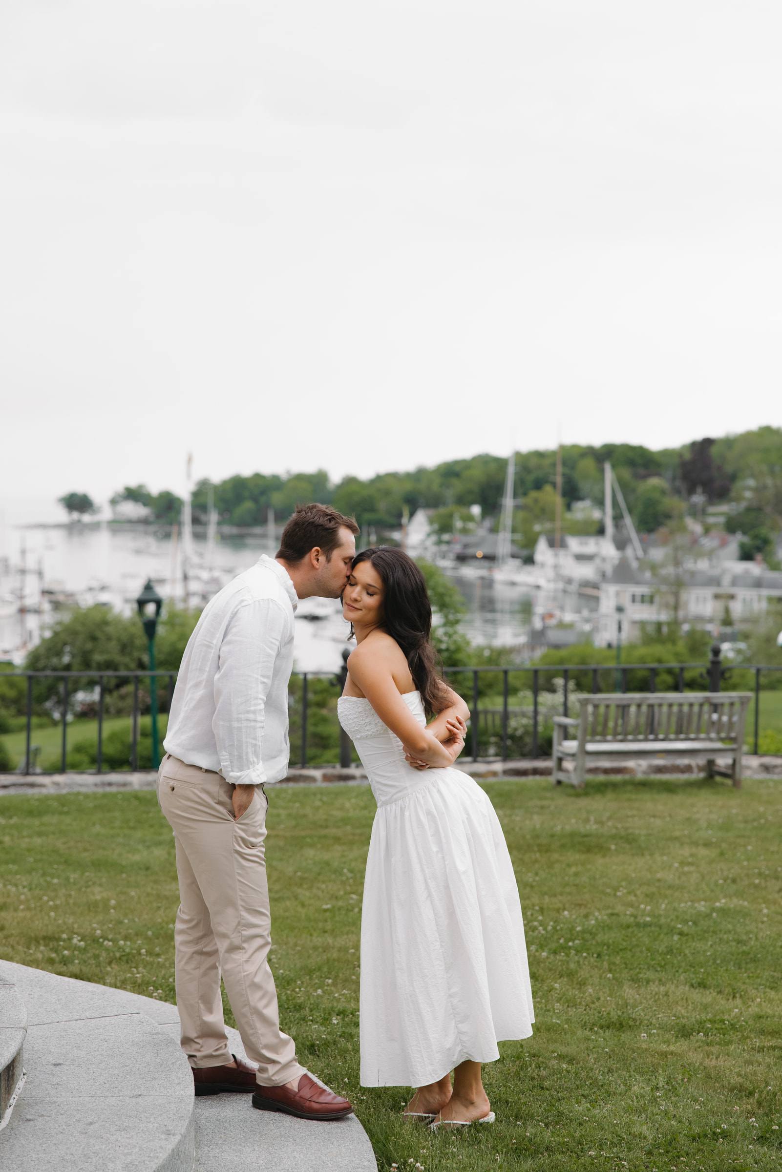 A couple sharing a kiss on a lawn above a harbour