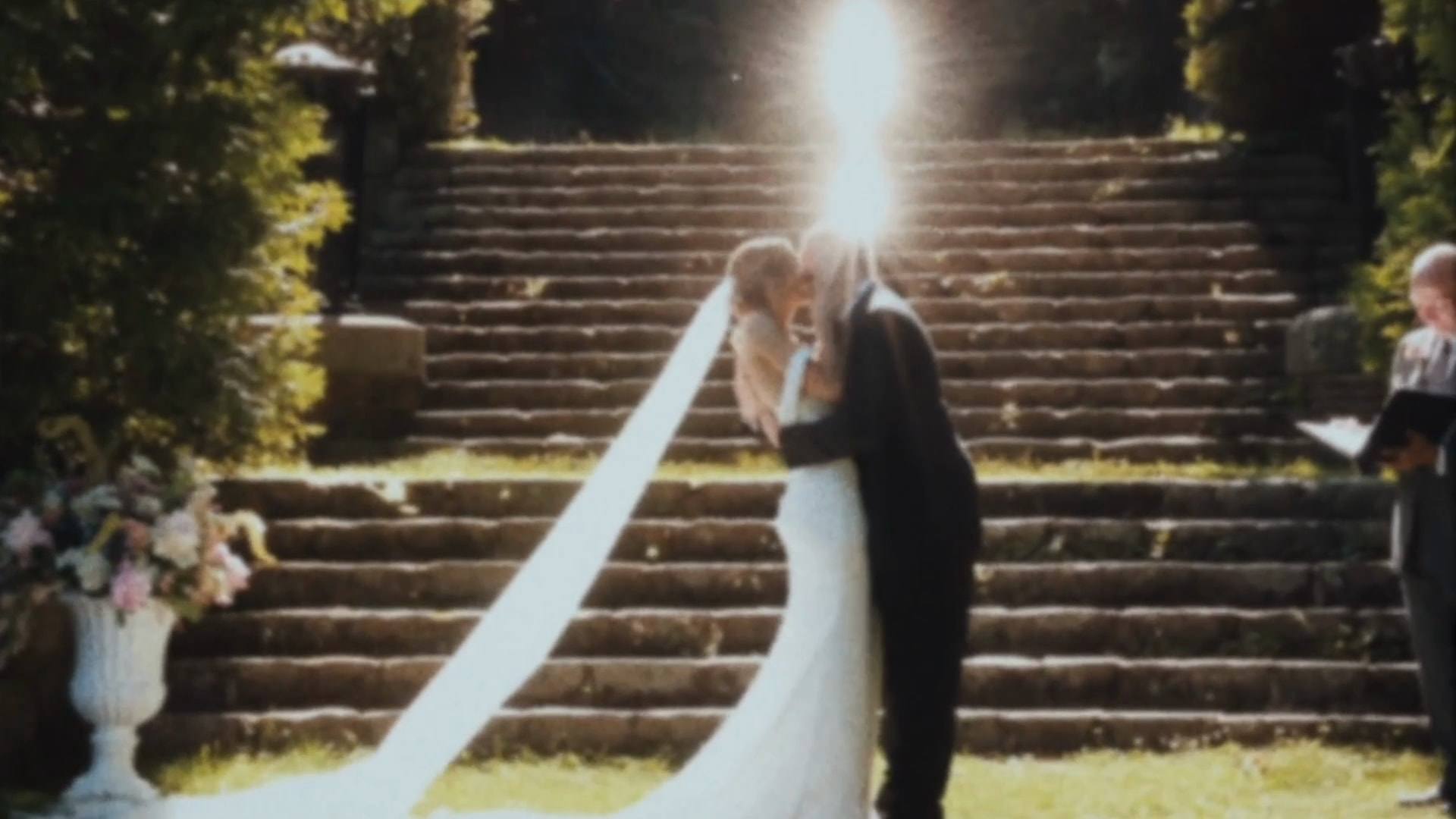 A bride and groom kissing at the ceremony steps with a long veil trailing, from a Super8 film