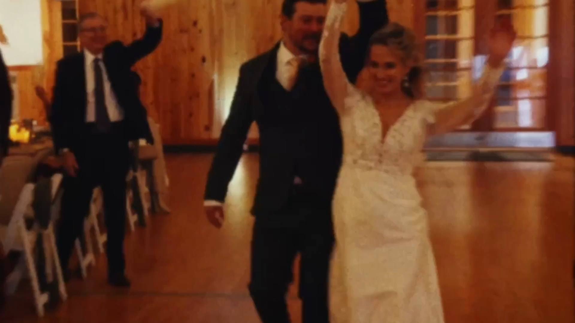 Newlyweds entering their reception with arms raised as guests cheer, from a Super8 film