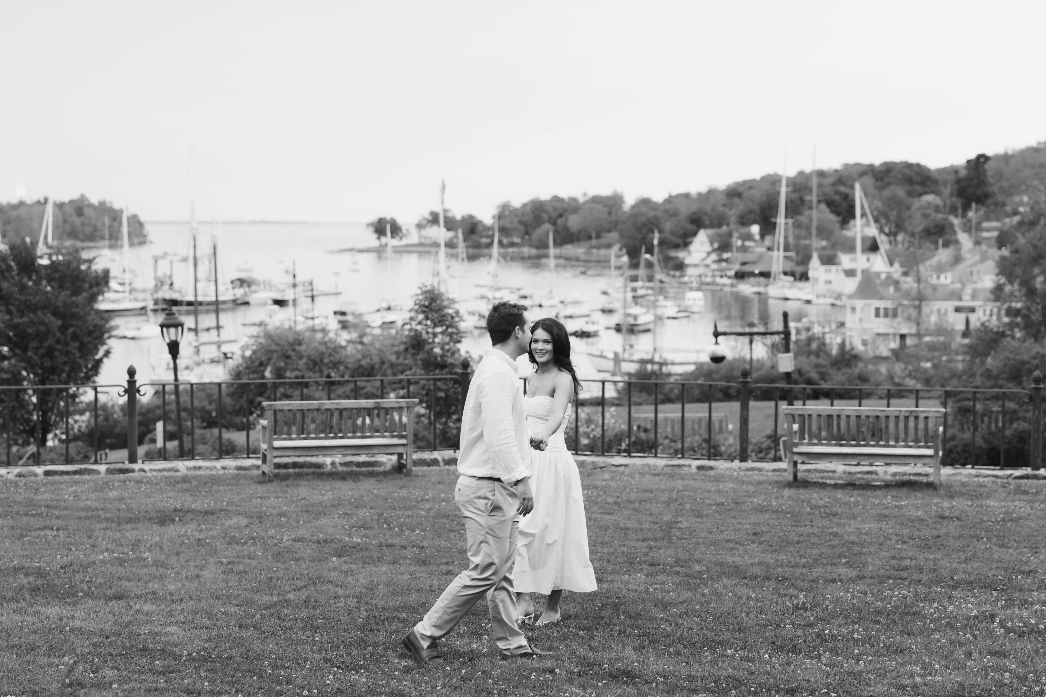 A couple walking hand in hand on a lawn above a harbour, in black and white