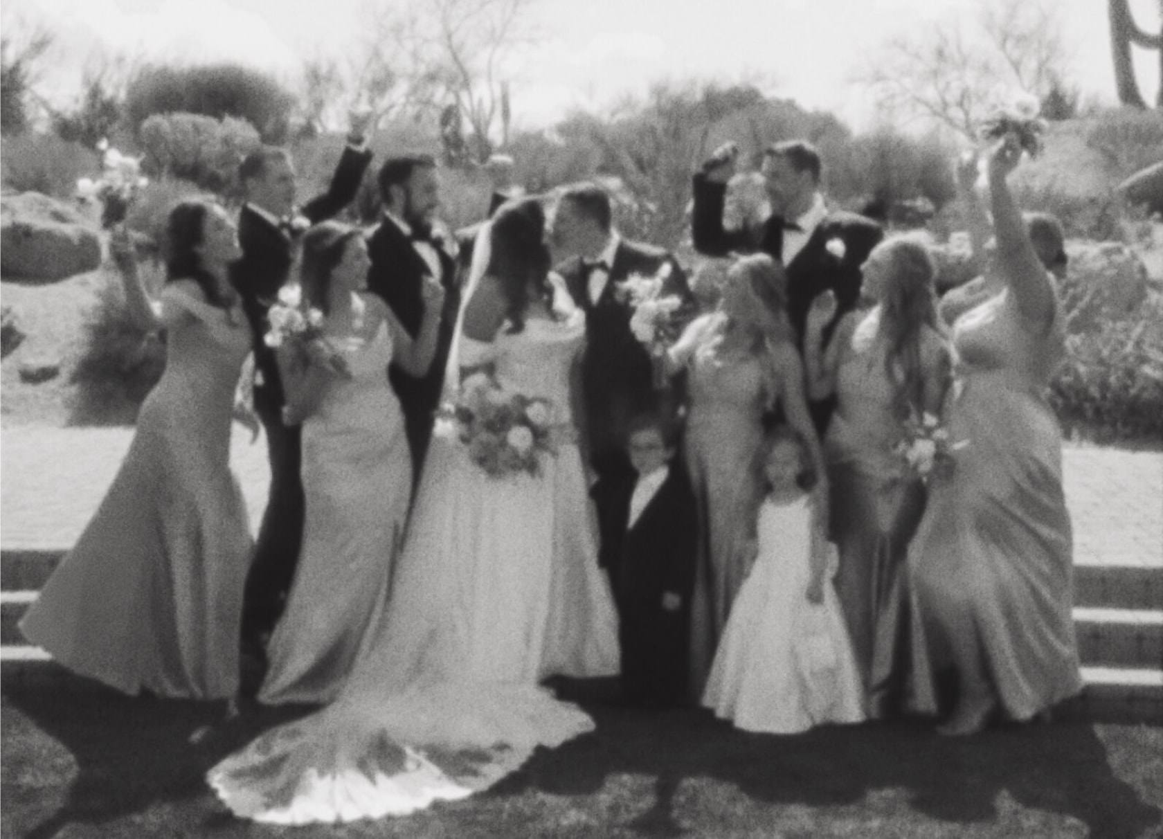 A wedding party cheering around the kissing couple, in black and white